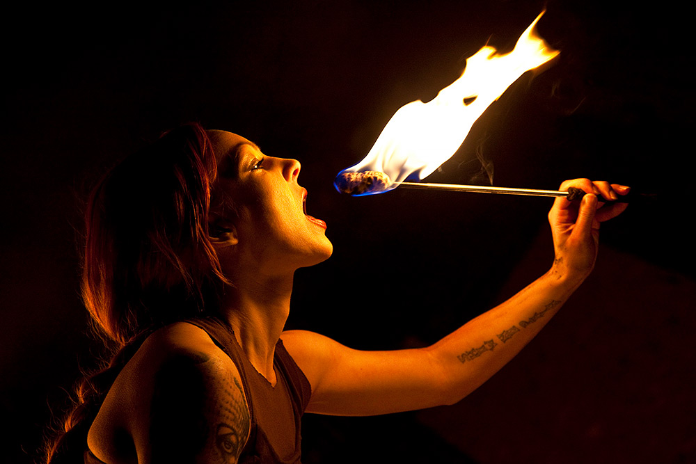 Kvinna i profil som gapar, hon ska sluka eld från en brinnande fackla.