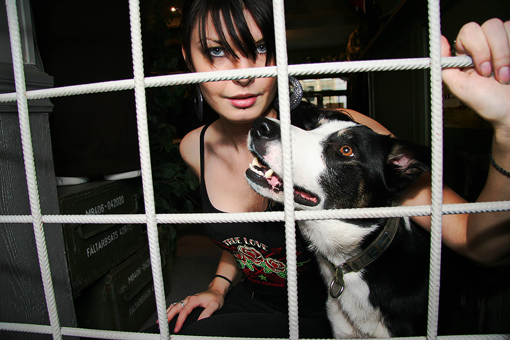 halvkroppsbild av en kvinna med svartvit hund står bakom ett vitt galler