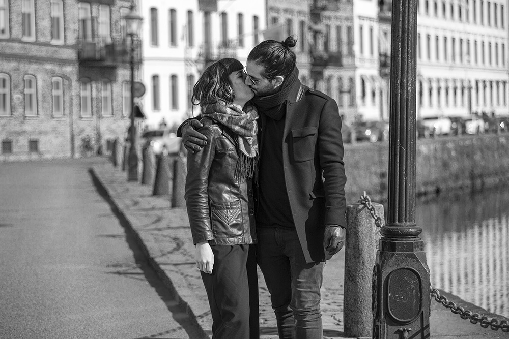 en mna och kvinna kysser varandra i stadsmiljö vid gamla hus och en kanal i Göteborg