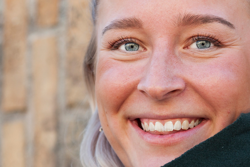 bild på del av ansikte av ung vit kvinna med stort leende, vita tänder, blå ögon och ljust hår
